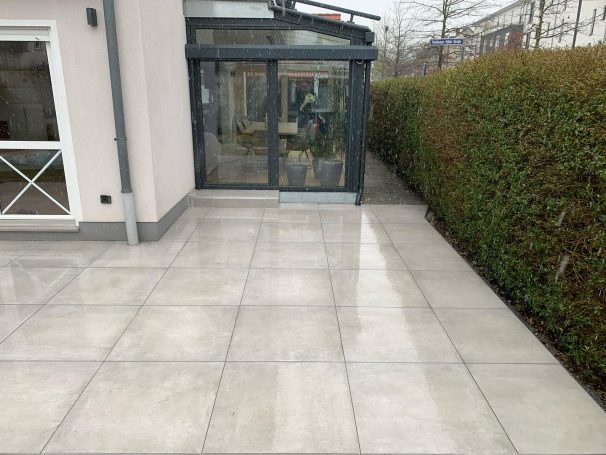 Gleichmäßige, helle Fliesenfläche neben einem modernen Wintergarten.