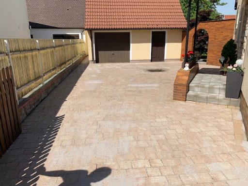 Gepflasterter Außenbereich mit Einfahrt und angrenzendem Garten.