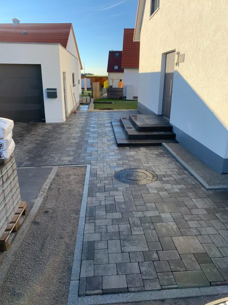 Angepasster Gehweg mit Pflastersteinen neben einem modernen Gebäude und einer Garage.