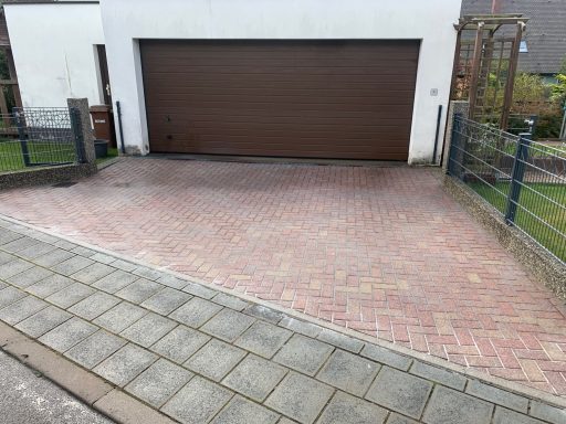 Ein gepflasterter Garagenvorplatz mit brauner Garagentür und Sichtschutzzaun.