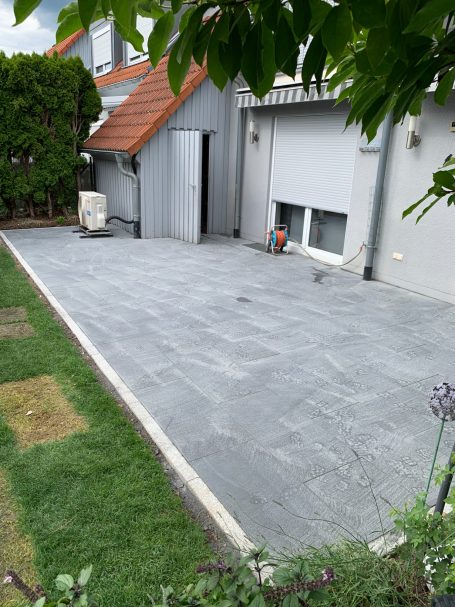 Gepflasterter Außenbereich mit grünem Rasen und einer Gebäudefassade im Hintergrund.