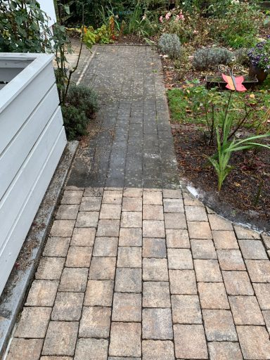 Pflasterweg im Garten, mit deutlich sichtbaren unterschiedlichen Belägen und Pflanzenbeeten.