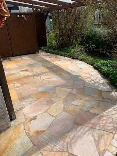 Natursteinterrasse mit unregelmäßigen Platten in einem begrünten Außenbereich.