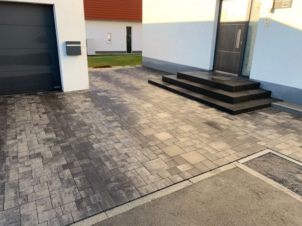 Eingang mit Treppe und gepflastertem Weg vor einem modernen Gebäude.