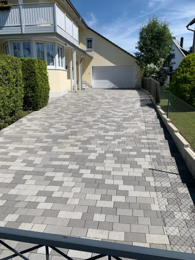 Pflastersteinerne Einfahrt mit gleichmäßigen Mustern vor einem Haus.