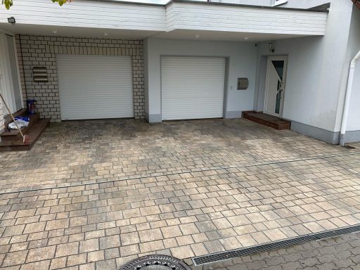 Garage und gepflasterter Parkplatz vor einem Wohngebäude.