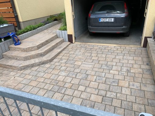 Pflasterfläche mit Treppenaufgang und geparktem Auto in einer Garage.