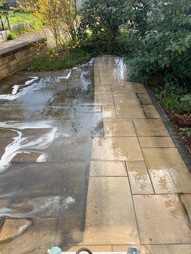 Nasser Gehweg mit gewaschenen und ungewaschenen Steinplatten, umgeben von Bäumen.